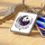 Trousseau de clés rectangulaire à cadre argenté présentant une surface blanche avec un design de lune croissante noire et violette complexe entourée de feuillage, d'étoiles et du texte ’les bois d’aurore’ sur une bannière.