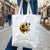 Sac fourre-tout en toile blanche orné d'un logo de tête de bélier en or et noir avec le texte 'bêhemora joaillerie' imprimé en dessous.